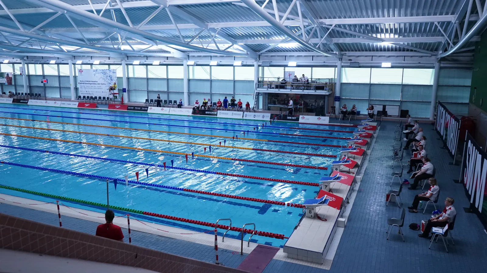 The Welsh National Pool in Swansea set up for the Swim Wales Summer Championships, showing the eight-lane competition pool and officials poolside.
